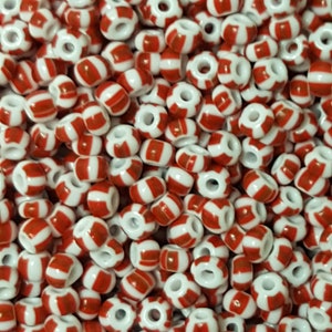 May include: A large quantity of small, white and red striped glass beads. The beads are round and have a hole in the centre.