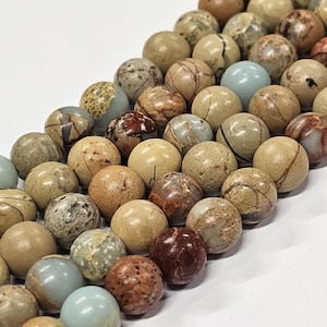 May include: A selection of spherical, natural stone beads in a range of earthy hues. The beads are polished, showcasing unique patterns of brown, beige, and grey. Some have a marbled look, while others are a solid colour.