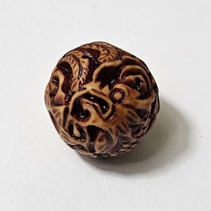 以下が含まれることがあります： 複雑な彫刻が施された丸い茶色のビーズ。ビーズは薄い茶色で、濃い茶色の模様があります。