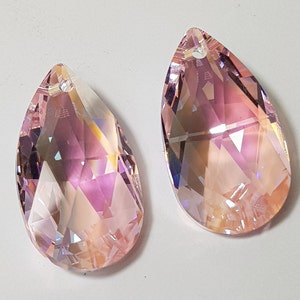 May include: Two teardrop-shaped crystal pendants with a pink iridescent finish. The pendants have a faceted design and a hole at the top for hanging.