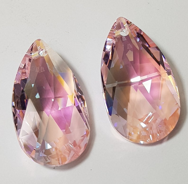 May include: Two teardrop-shaped crystal pendants with a pink iridescent finish. The pendants have a faceted design and a hole at the top for hanging.