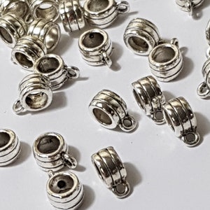 May include: A collection of silver-toned metal bead caps with a decorative grooved design. Each cap features a small loop at the top for attaching to jewellery.