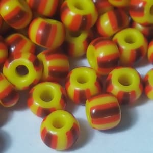 May include: A close-up of a pile of yellow and red striped beads. The beads are made of plastic and have a glossy finish.