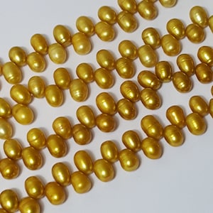 Puede incluir: Una hebra de perlas doradas, dispuestas en un patrón escalonado. Las perlas son lisas y tienen un alto brillo.