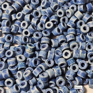 May include: A large pile of blue ceramic beads with a speckled, denim-like finish. The beads are all the same size and shape, and they are arranged in a random pattern. The beads are ideal for jewellery making or other craft projects.