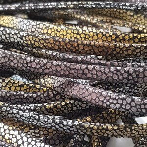 May include: Close-up of a pile of black, silver, and gold leather cord. The cord has a textured, embossed pattern that resembles scales.