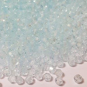 May include: A large pile of small, clear, faceted glass beads with a light blue tint. The beads are round and have a slightly textured surface.