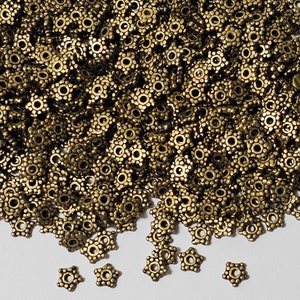 May include: A large pile of antique gold metal star-shaped beads. The beads have a raised, textured surface and a small hole in the center.