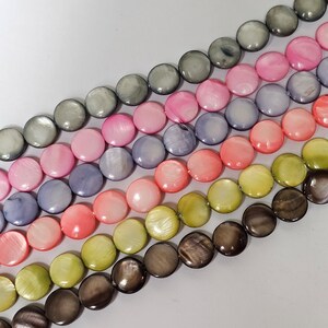 Könnte beinhalten: Eine Reihe runder, flacher, irisierender Muschelkugeln in verschiedenen Farben, darunter Grau, Rosa, Lila, Pfirsich, Grün und Braun.