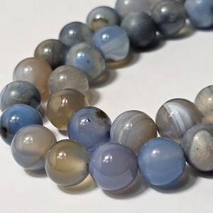 May include: A strand of blue agate beads with white and grey patterns. The beads are round and smooth, and they are strung on a clear thread.