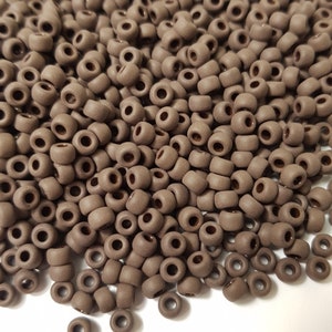 May include: A large pile of brown seed beads. The beads are small and round, and they are all the same size. They are ideal for making jewellery or other crafts.