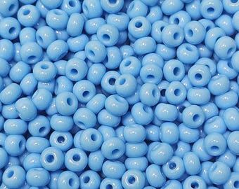 Può includere: Un'immagine ravvicinata di una grande quantità di piccole perline di vetro di colore blu chiaro. Le perline sono rotonde e hanno una finitura liscia e lucida.