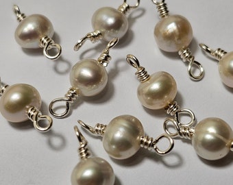 May include: A close-up of ten pearl and silver bead charms. The pearls are off-white and the silver beads are wrapped around the pearls.