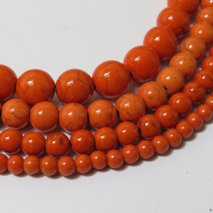 May include: A strand of orange beads in various sizes. The beads are round and have a smooth, polished finish.