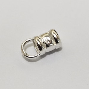 May include: A small, shiny silver jewellery finding with a loop and a cylindrical body. The body has a ribbed texture and a small marking. It is likely used for attaching clasps or other components in jewellery making.