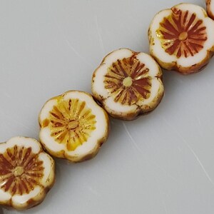 May include: A string of white ceramic flower beads with brown and yellow accents. The beads are round and have a raised flower design.