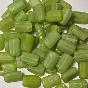 Könnte beinhalten: Eine Sammlung grüner Glasperlen mit weißen Streifen. Die Perlen sind rechteckig und haben eine glänzende Oberfläche.