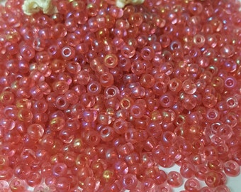 May include: A large pile of small, round, iridescent pink beads. The beads have a translucent quality and are perfect for jewellery making.