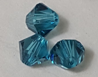 May include: Three teal blue faceted glass beads. The beads are round and have a starburst pattern.