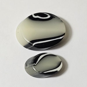 May include: Two oval-shaped buttons with a black and white swirl pattern. The larger button is white with black swirls, and the smaller button is grey with black swirls.