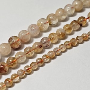 May include: Three strands of clear quartz beads with golden and red inclusions. The beads are round and have a smooth, polished finish.
