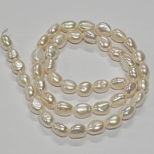 Pode incluir: Um fio de pérolas de água doce de cor esbranquiçada, com formas barrocas e irregulares. Cada pérola apresenta uma superfície iridescente de alto brilho com contornos orgânicos únicos, enfiadas num fio branco fino em espiral.