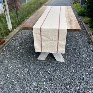May include: A rustic wooden table with a white painted base and a red and white striped linen table runner.