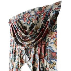 May include: A floral valance with a cream background. The valance features a repeating pattern of large flowers in shades of red, blue, green, and yellow. The fabric is draped and gathered, creating a decorative window treatment.