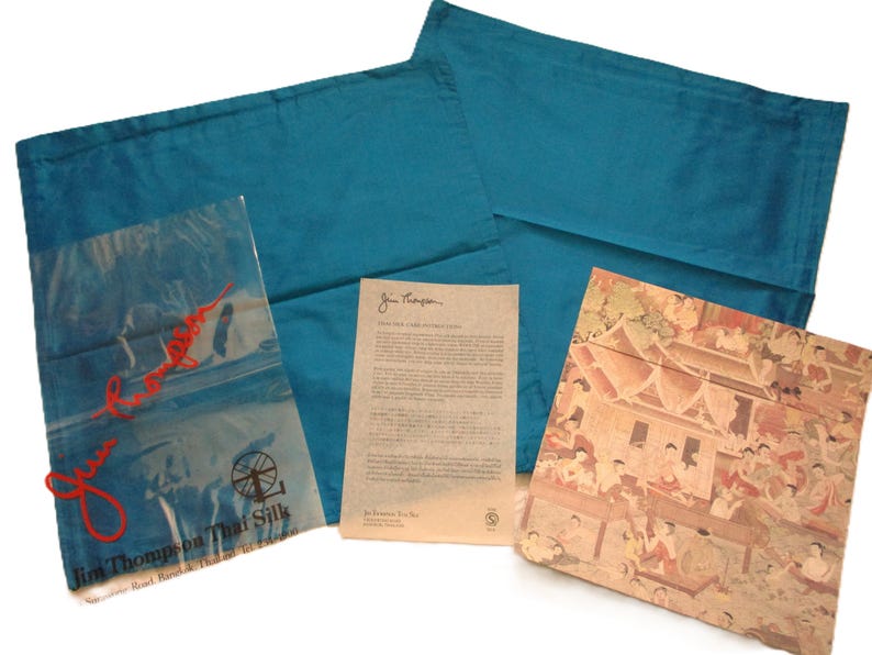 May include: Teal-colored pillowcases with a matching package and a printed card. The package is clear with red text and a logo. The card has printed text. A decorative card with a detailed illustration is also included.