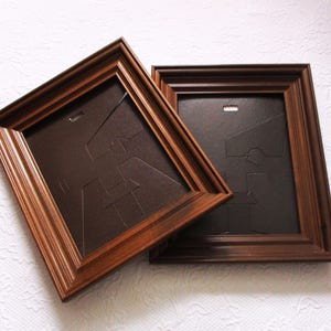 May include: Two rectangular picture frames with dark brown wood-toned borders and stepped molding. Each frame features a dark brown backing board with a built-in easel stand and a metal hanging tab visible on the rear side of the frame structure.