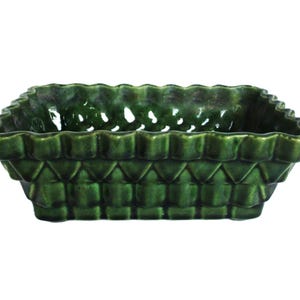 May include: A dark green ceramic planter, rectangular in shape, with a woven basket design. It has a scalloped rim and a glossy finish. The sides display a repeating diamond pattern. Suitable for small plants or succulents.