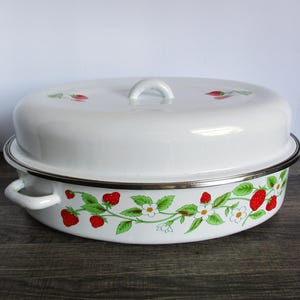 May include: White enamelware oval roaster with a lid. The roaster features a decorative strawberry vine design with red strawberries, green leaves, and white flowers. The lid has a white handle and strawberry accents.
