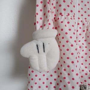 以下が含まれることがあります： 白いピンクのドット柄のドレスで、白い手袋型の袖が特徴です。ドレスの裾には白いレースのトリムがあり、前面にはジッパーが付いています。ピンクのドットは明るい色です。