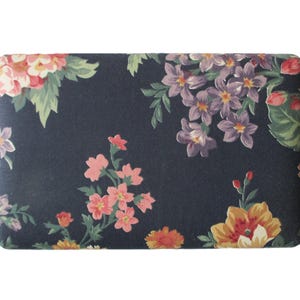 May include: A rectangular fabric piece featuring a dark navy blue background with a floral pattern. The print includes clusters of pink, yellow, and purple flowers with green leaves scattered across the surface in a repeating botanical arrangement.