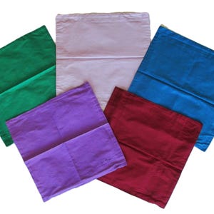 May include: A collection of five square fabric cushion covers arranged in a fan shape. The covers are solid colours including green, light pink, blue, purple, and dark red. Each square cover features a horizontal seam across the middle section.