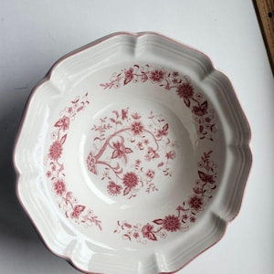 May include: White ceramic serving bowl with a scalloped edge and a floral pattern in shades of red. The bowl has a wide rim and a deep center, suitable for serving various dishes. The floral design is detailed and covers the interior surface.