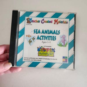 May include: A CD-ROM case for "Sea Animals Activities" by Teacher Created Materials. The cover features a blue and white striped background with illustrations of fish and a seahorse. Text includes "Ages 5-9" and "Kid Pix Activity Kit."