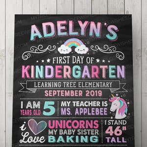 May include: A black chalkboard-style sign with colorful text and graphics. It reads "Adelyn's First Day of Kindergarten" with a rainbow and cloud graphic. Includes details about the child, including height of 46 inches, age, and favorite things.