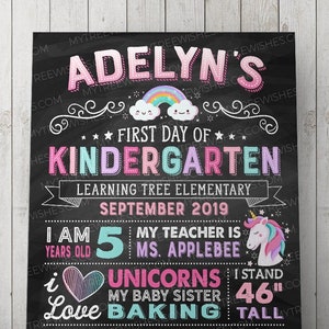 May include: A chalkboard-style sign with the text "Adelyn's First Day of Kindergarten." It includes a rainbow, a unicorn, and the text "I stand 46" tall." The sign also lists the child's age, teacher, and favorite things.