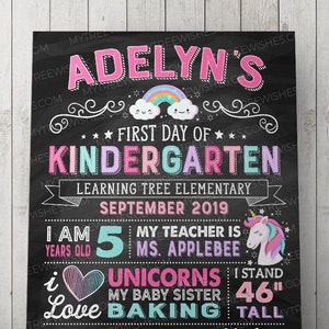 May include: A black chalkboard-style sign with colorful text and illustrations. It reads "Adelyn's First Day of Kindergarten" with a rainbow and cloud graphic. Includes details about the child's age, teacher, and favorite things. The sign is 46 inches tall.