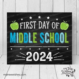 May include: Black chalkboard sign with white text that reads "First Day of Middle School 2024". The sign is decorated with green apples and stars.