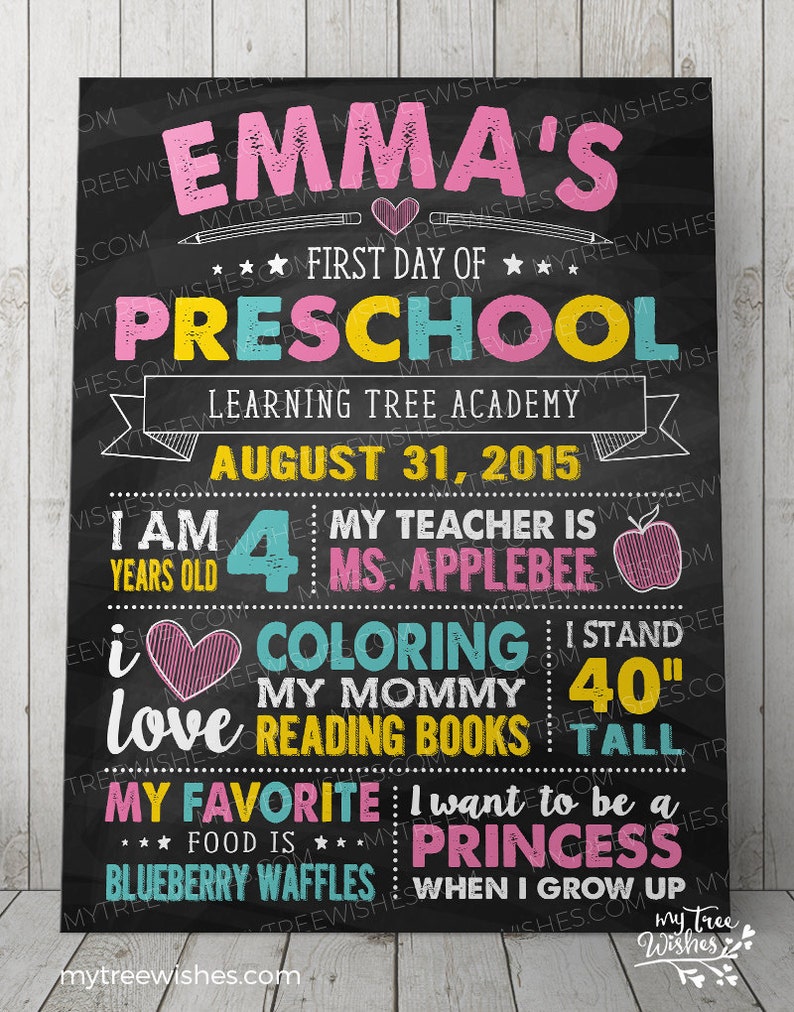 May include: A black chalkboard sign with colorful text announcing a child's first day of preschool. The sign says "Emma's First Day of Preschool" and includes details like the child's age, teacher's name, and favorite things.