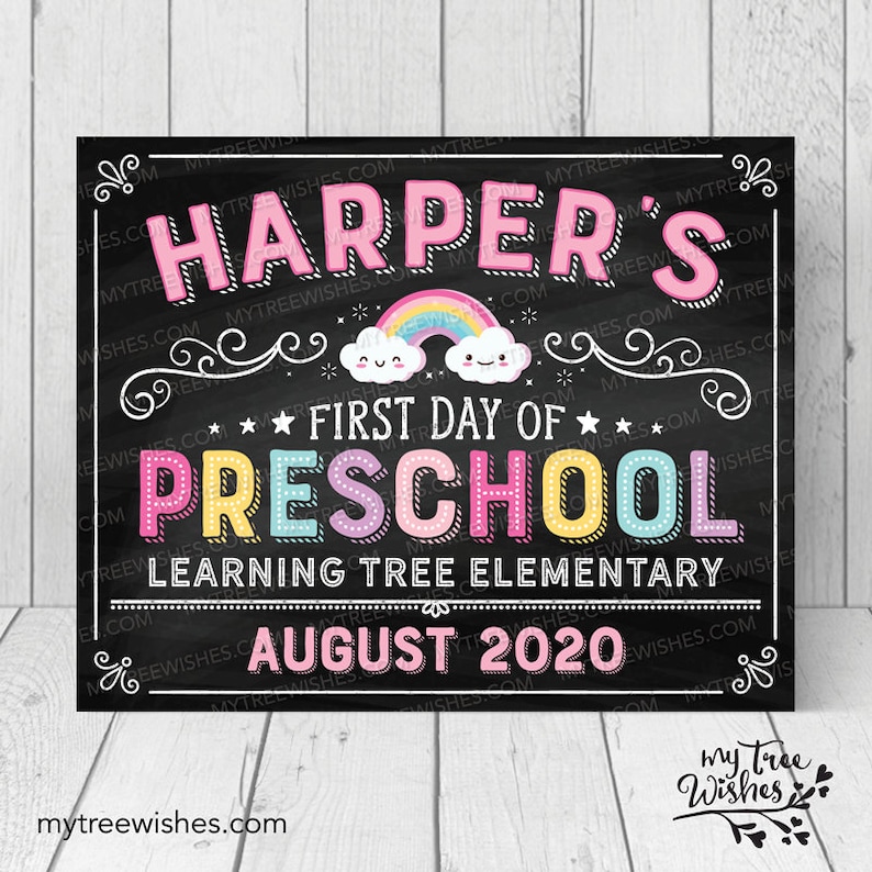 May include: A chalkboard-style sign with the text "Harper's First Day of Preschool" in colorful letters. A rainbow and smiling clouds are featured above the word "Preschool". The sign also includes the text "Learning Tree Elementary" and "August 2020".