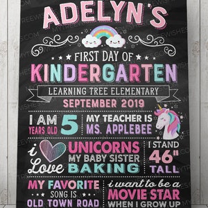 May include: A chalkboard-style sign with the text "Adelyn's First Day of Kindergarten." It includes a rainbow, unicorn, and the text "I stand 46" tall." The sign also lists the child's age, teacher, and favorite things.