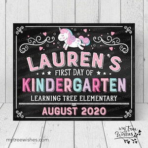 May include: A chalkboard-style sign with the text "LAUREN'S FIRST DAY OF KINDERGARTEN" in pink, blue, and white. A cartoon unicorn is at the top. The sign also includes the text "LEARNING TREE ELEMENTARY" and "AUGUST 2020".