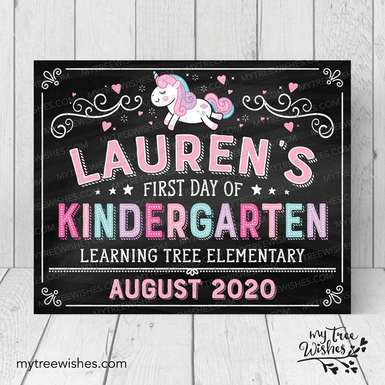 May include: A chalkboard-style sign with the text "LAUREN'S FIRST DAY OF KINDERGARTEN" in pink, blue, and white. A cartoon unicorn is at the top. The sign also includes the text "LEARNING TREE ELEMENTARY" and "AUGUST 2020".