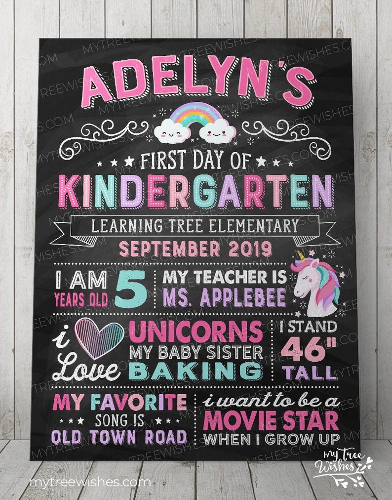 May include: A black chalkboard-style sign with colorful text and illustrations. It reads "Adelyn's First Day of Kindergarten" with a rainbow and cloud graphic. Includes details about the child's age, teacher, and favorite things. The sign is 46 inches tall.