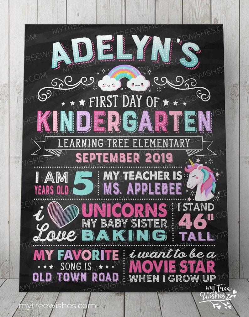 May include: A black chalkboard sign with colorful text announcing "Adelyn's First Day of Kindergarten." Includes a rainbow, unicorn, and the text "I stand 46" tall." The sign also lists the school, teacher, and favorite things.