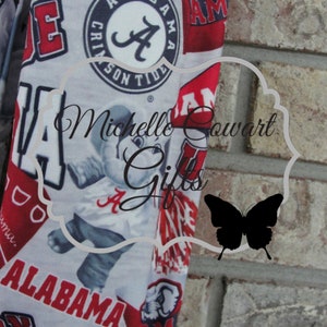 May include: Fabric with a repeating pattern of red and white Alabama Crimson Tide logos, text, and imagery. The design includes the word "ALABAMA" and the team's logo. The background is a light gray color.