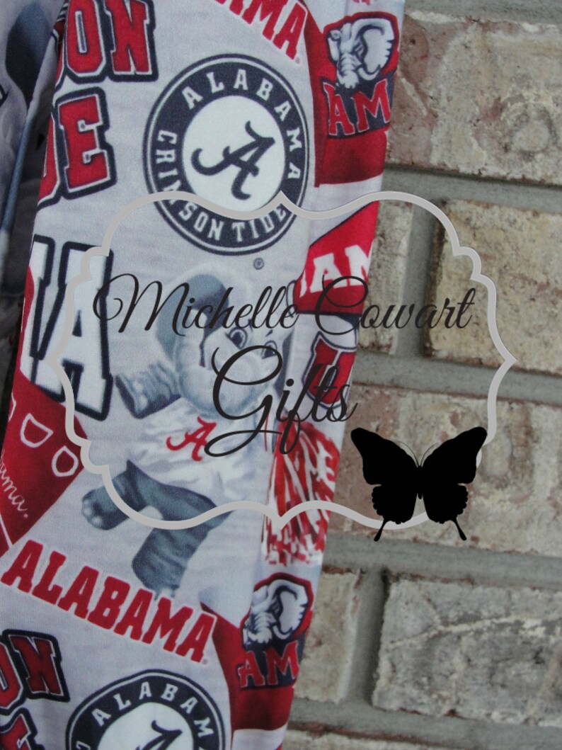 May include: Fabric with a repeating pattern of red and white Alabama Crimson Tide logos, text, and imagery. The design includes the word "ALABAMA" and the team's logo. The background is a light gray color.